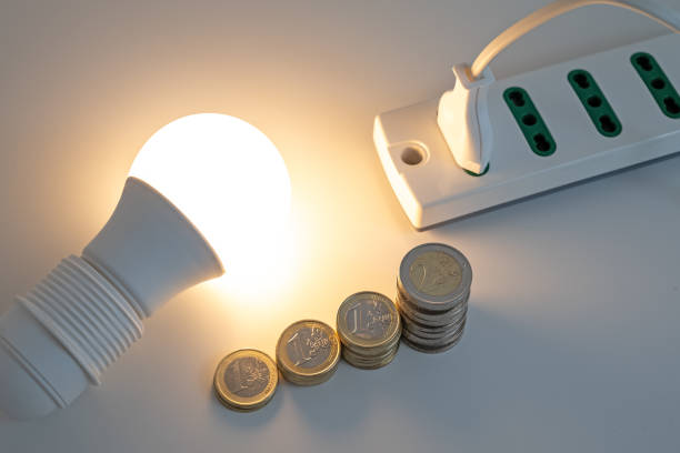 Light bulb on, with plug and coins next to it. Energy costs. stock photo