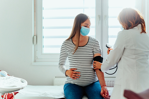Médico con una mujer embarazada usando máscaras médicas durante un examen photo