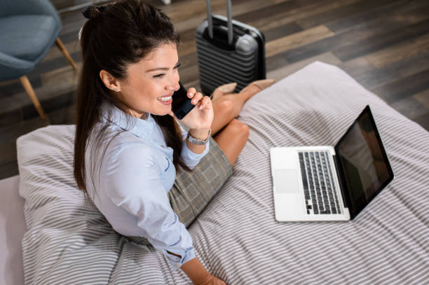 mujer de negocios en habitación de hotel en viaje de negocios sentada en la cama usando un teléfono inteligente. - working bed smart phone bedroom fotografías e imágenes de stock