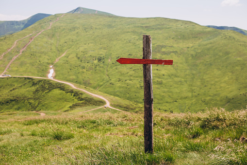One wooden red signpost in the summer mountain with copyspace. Conceptual leading indicator. Arrow on the wooden signpost pointing to a direction.