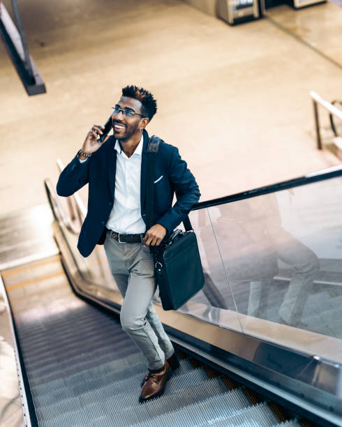istock Smiling young black businessman using his smartphone on an escalator, vertical 1366945147