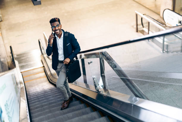 istock Smiling young black businessman using his smartphone on an escalator 1366945148