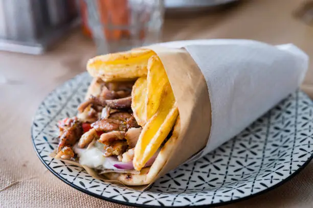 Traditional Greek food gyros pita with fries, vegetables and tzatziki sauce. Close up of kebab sandwich in Crete, Greece. Traditional Greek cuisine.