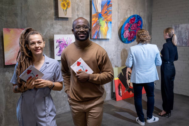 Young couple visiting exhibition in gallery Young happy couple with brochures walking along the art gallery and looking at paintings art museum stock pictures, royalty-free photos & images