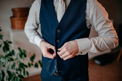 Details of the groom buttoning his vest during his preparations