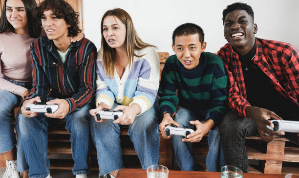 Multiracial young friends having fun playing video games at home - Focus on asian boy face stock photo