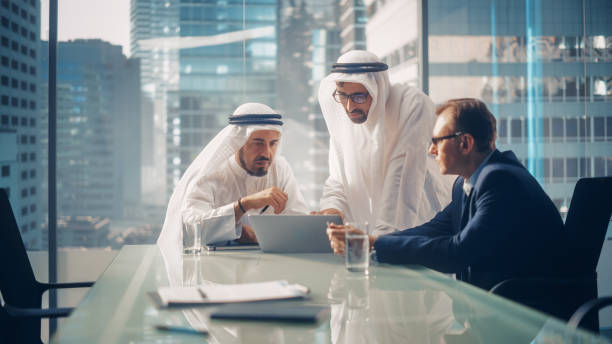 International Business Consultant Advises on Financial Strategy Plan to Successful Arab Company Owners. Multicultural Meeting in Modern Office Between American and Saudi Businessman. International Business Consultant Advises on Financial Strategy Plan to Successful Arab Company Owners. Multicultural Meeting in Modern Office Between American and Saudi Businessman. middle eastern clothes stock pictures, royalty-free photos & images
