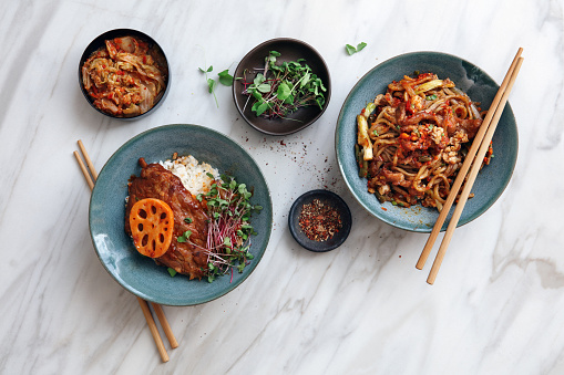 Spicy Korean beef noodles (Shin Ramyun). Korean BBQ pork ribs with rice. Flat lay top-down composition on marble background.