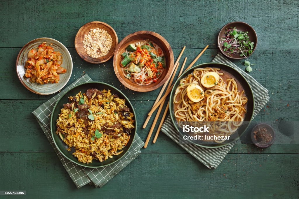 Korean Dishes Dan Dan Noodles (Tantanmen Ramen or Tan Tan Noodles). Korean-style Curry Beef Fried Rice. Flat lay top-down composition on dark green background. Chinese Food Stock Photo