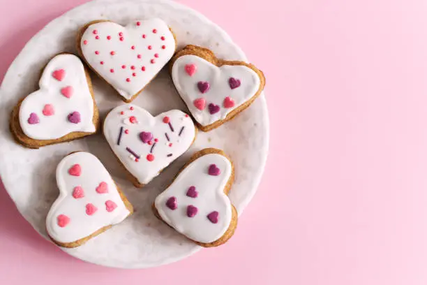 Gingerbread covered with white icing and sprinkling on a white saucer on a pink background. The concept of celebrating Valentine's Day. Horizontal orientation. copy space. Top view.
