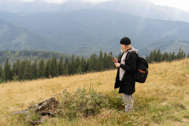 girl traveler on vacation in nature and plans an online route map in a smartphone, a tourist girl uses a mobile phone enjoying her vacation against the backdrop of a mountain panorama Baner copy space chica viajera con sombrero mientras está de vacaciones en la naturaleza y planea un mapa de ruta en línea en un teléfono inteligente, una niña turista usa un teléfono móvil disfrutando de sus vacaciones con el telón de fondo de un panorama de monta�
