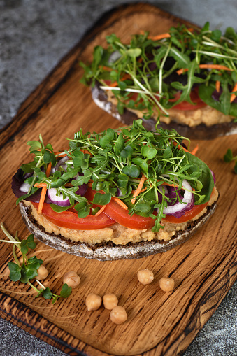 Sandwich toasted rustic bread with chickpea hummus, tomato slices, mix of lettuce and microgreens. Vegetarian breakfast.