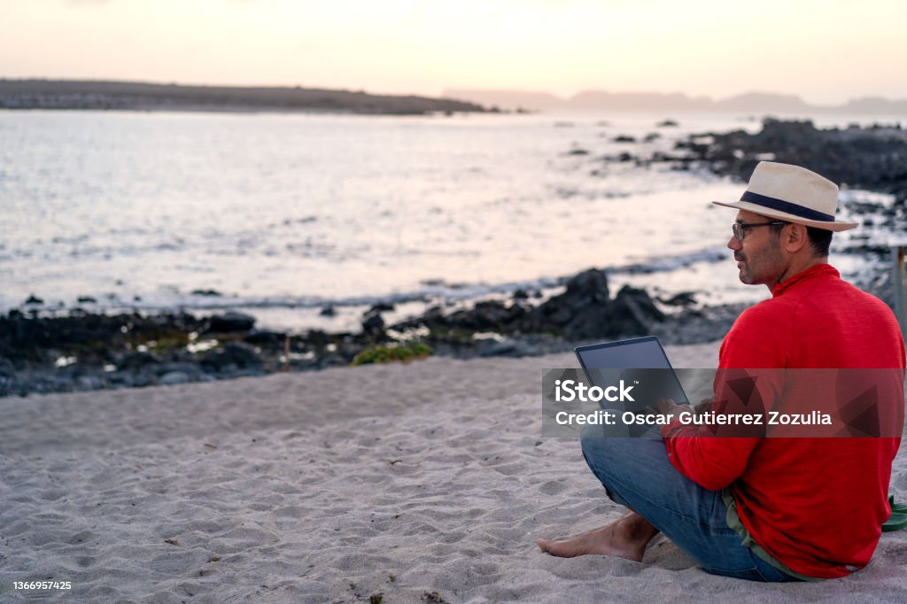 man sitting on the beach outdoor with a laptop alone doing telecommuting or remote work, back view Beach Stock Photo