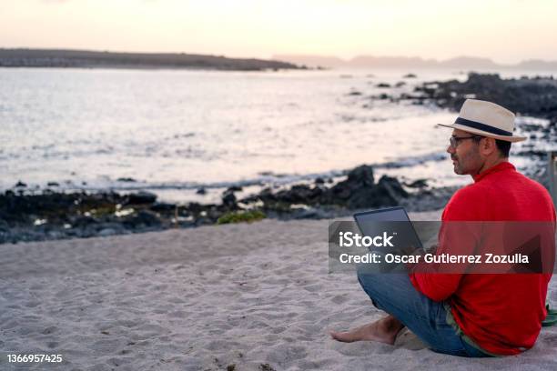 Man Sitting On The Beach Outdoor With A Laptop Alone Doing Telecommuting Or Remote Work Back View Stock Photo - Download Image Now
