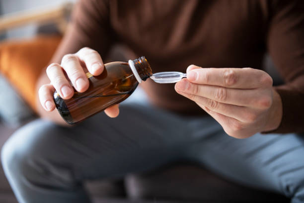 man pouring cough syrup into spoon. - maple imagens e fotografias de stock