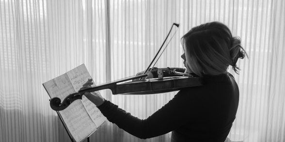 Musician playing violin at her home near the window, practicing on the beautiful sunny day. Stock photography