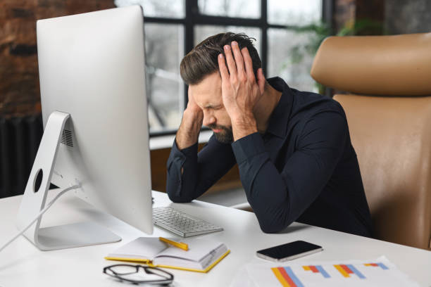 istock Tired caucasian guy sitting at the table. Frustrated pensive man worried about work issues, covering head with hands in front of the computer 1366966092