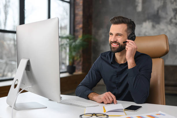 concept d’employés de bureau. un homme caucasien concentré portant un casque sans fil utilise un ordinateur portable pour une conversation vidéo en ligne, parler avec des clients ou des collègues - service computer training office photos et images de collection