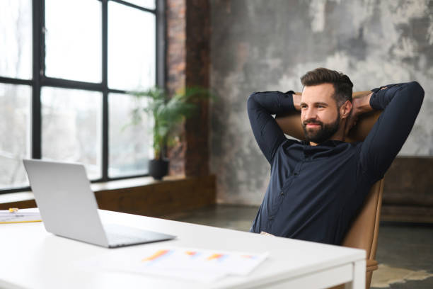 istock Unshaved man sitting at the table and smiling, while feeling comfort and relaxation at his workplace. Confident worker sitting in front of the laptop 1366967133