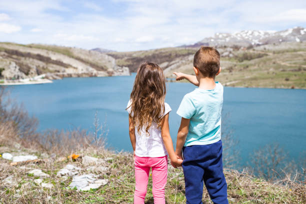 Group of children sitting on the edge of the mountain, having a break after long walk in the forest.