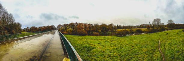A panoramic picture from a bridge to a field with horses and a river.