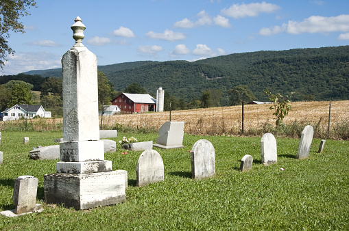 Country cemetery under fair weather summer skies with mountains and farm behind, rural Pennsyvania, PA, USA.