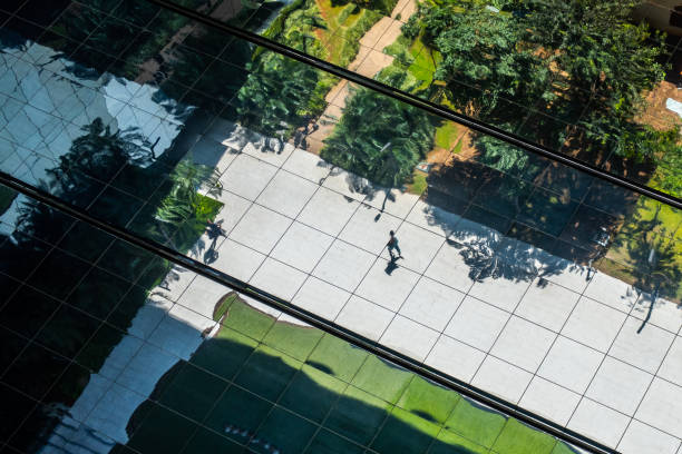 Spiegelbild einer Person, die zwischen Gärten in einem Finanzzentrum einer Großstadt spaziert