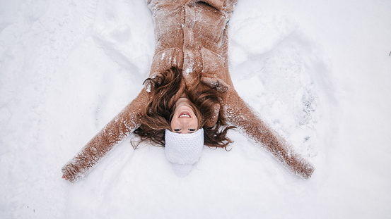 A young woman falling into snow, making an angel in snow and laughing