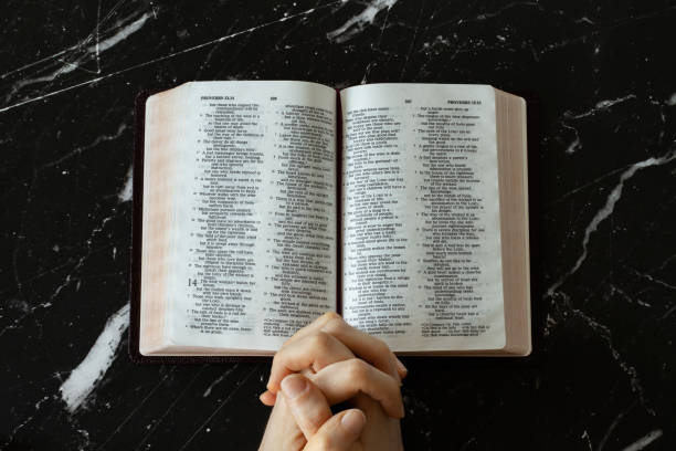 istock Praying hands folded in prayer to God Jesus Christ with open Holy Bible Book 1366976263