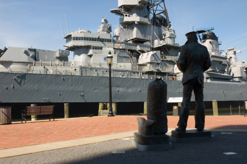 Navy sailor statue and USS Wisconsin battleship at harbor dock at dawn, vintage US Navy WW2 military display, a tourist destination in Norfolk, Virginia, VA, USA.