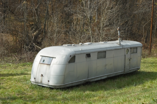 Mobile home trailer abandoned and parked in the grass, fifties retro style in silver metal.