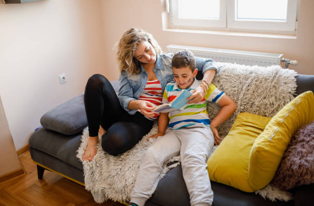 istock Young mother reading book to her son on sofa at home 1366977652