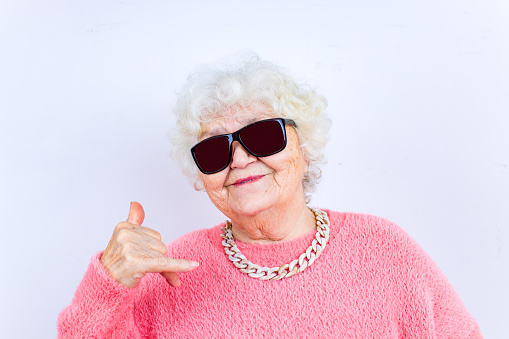 Retrato de una divertida mujer rubia mayor con gafas de sol y suéter rosa sobre fondo blanco photo