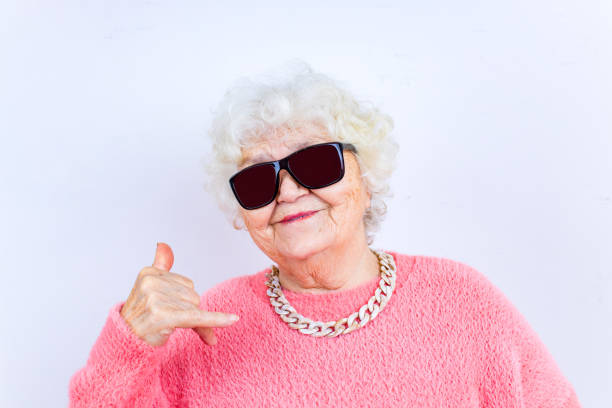 portrait d’une drôle de femme blonde senior en lunettes de soleil et pull rose sur fond blanc - seulement des femmes seniors photos et images de collection