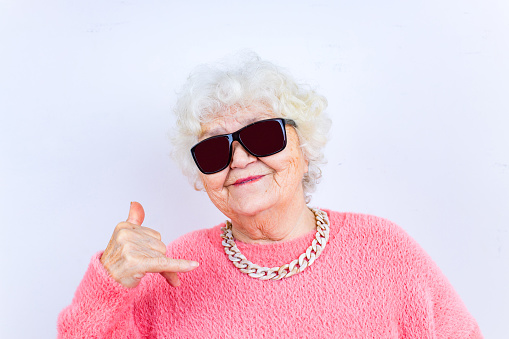 Portrait of funny senior blonde woman in sun glasses and pink sweater on white background.