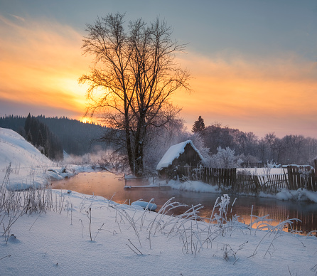 house in village near the river against the backdrop of the mountains on a winter evening at sunset