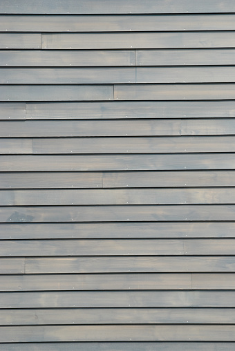 New clapboard house siding with thin gray paint wash, nailheads showing for wood backgrounds.