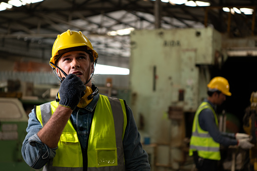 Chief mechanical engineer working in a mechanical factory make radio communication control with walkie-talkie and follow up with Asian technicians who are repairing old machines.
