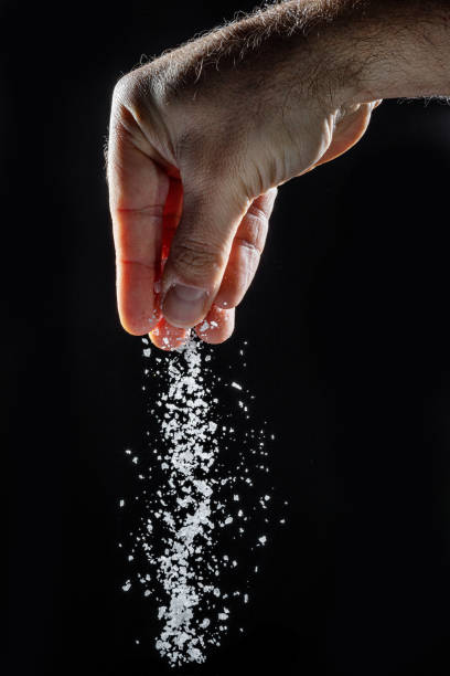 istock Male hand sprinkling edible salt at black background. 1366988565