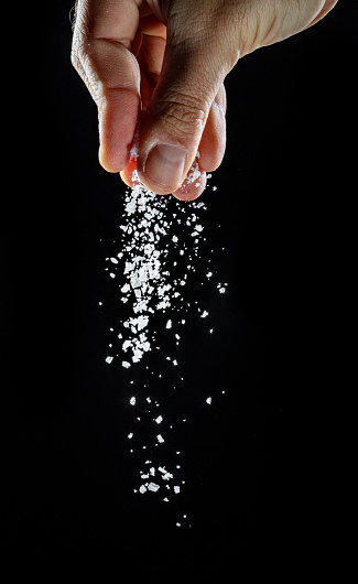 Male hand sprinkling edible salt at black background.