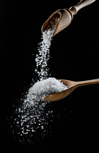 Edible salt crystals falling down into the wooden spoon at black background. stock photo