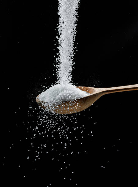 istock White refined sugar crystals falling down into the wooden spoon at black background. 1366988620