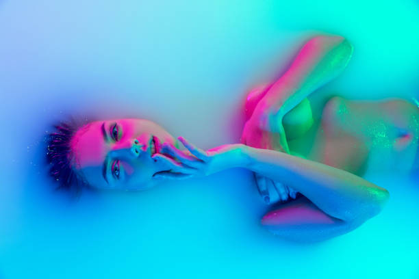 Top view of female face, young girl in the milk bath with soft glowing in blue-pink neon light. Beauty, fashion, style, skincare concept Attractive look. Top view of female face, young girl in the milk bath with soft glowing in blue-pink neon light. Copyspace for ad. Beauty, fashion, style, skincare concept. Tender woman with wet hair seductive women stock pictures, royalty-free photos & images