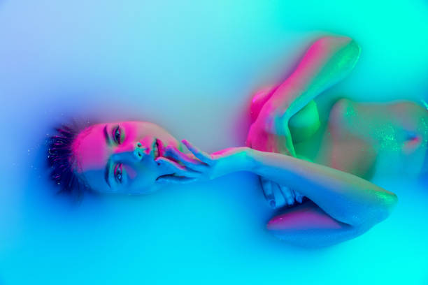 top view of female face, young girl in the milk bath with soft glowing in blue-pink neon light. beauty, fashion, style, skincare concept - förförisk kvinna bildbanksfoton och bilder