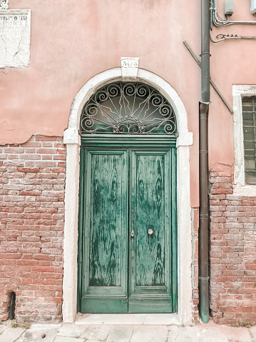 Green window on cracked concrete wall overlooking red bricks in Burano Island, Italy