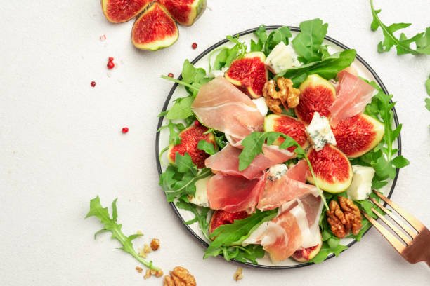 istock Fresh fig salad with prosciutto, gorgonzola, walnuts, arugula on white kitchen table background, top view, copy space 1366993497