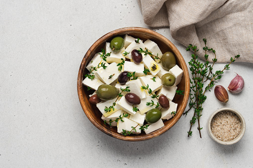 Soft feta cheese with olive oil, herbs and olives in wooden bowl on white background