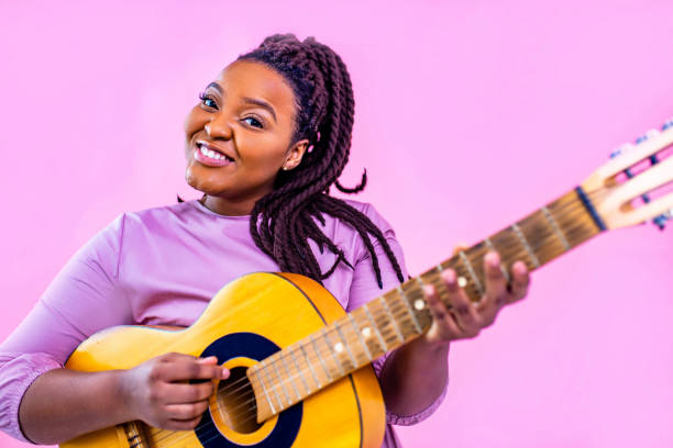 Young woman playing guitar on color pink studio background.