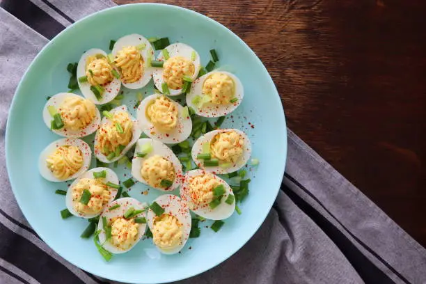 Deviled Eggs sprinkled with paprika and chopped green onion on a green plate on a woodene table . Top view .