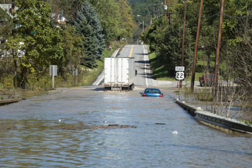 High water flash flooded highway emergency after a strong summer thunderstorm, one stranded car and a semi truck able to drive through amid floating debris, Pennsylvania, PA, USA.